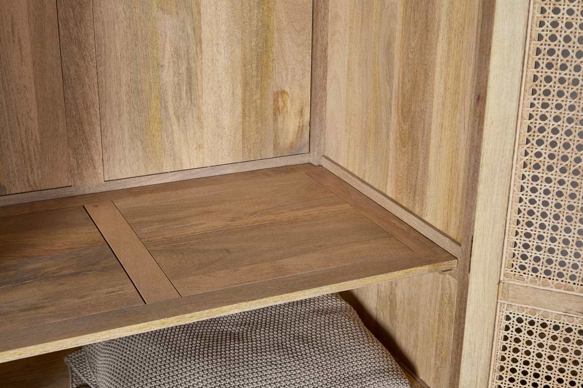 A close-up of the Kanz Mango Wood Wardrobe by nkuku showcases its natural mango wood grain shelf, woven rattan right door, and a textured light brown basket beneath, all highlighted by warm lighting.