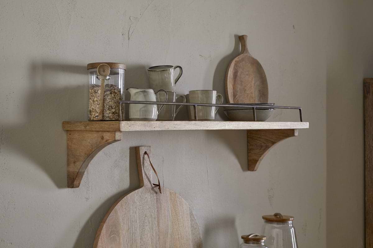 The nkuku Meera Mango Wood & Iron Gallery Shelf in Natural displays a glass jar with oats, ceramic cups, a creamer, and a tray. Below, two round cutting boards hang on the wall for rustic kitchen storage in neutral tones.