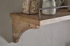 The nkuku Meera Mango Wood & Iron Gallery Shelf - Natural features a curved bracket, metal rail, and natural finish—ideal for kitchen storage. Shown holding a glass jar of oats and a white ceramic pitcher against a light wall.