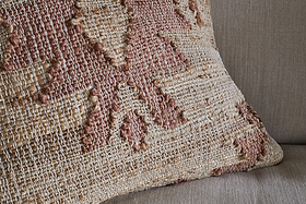 The Nila Gul Cushion Cover - Rust by nkuku showcases a geometric, southwestern-inspired pattern in earthy beige and muted rust tones. Its textured cotton and jute weave creates a rustic, artisanal look, perfect for accenting a taupe fabric couch.