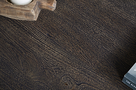 A close-up of nkuku's Sita Reclaimed Wood & Iron Coffee Table in Chocolate Brown highlights its striking grain. A wooden tray with a white object rests top left, while a black and white book peeks in from the bottom right corner.