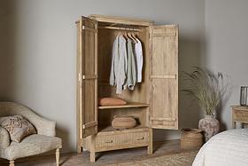 The nkuku Vivan Grooved Wardrobe - Natural features open doors displaying hanging clothes, a folded sweater, a woven basket on a shelf, and a closed drawer—offering elegant bedroom storage in serene neutral tones with soft natural light.