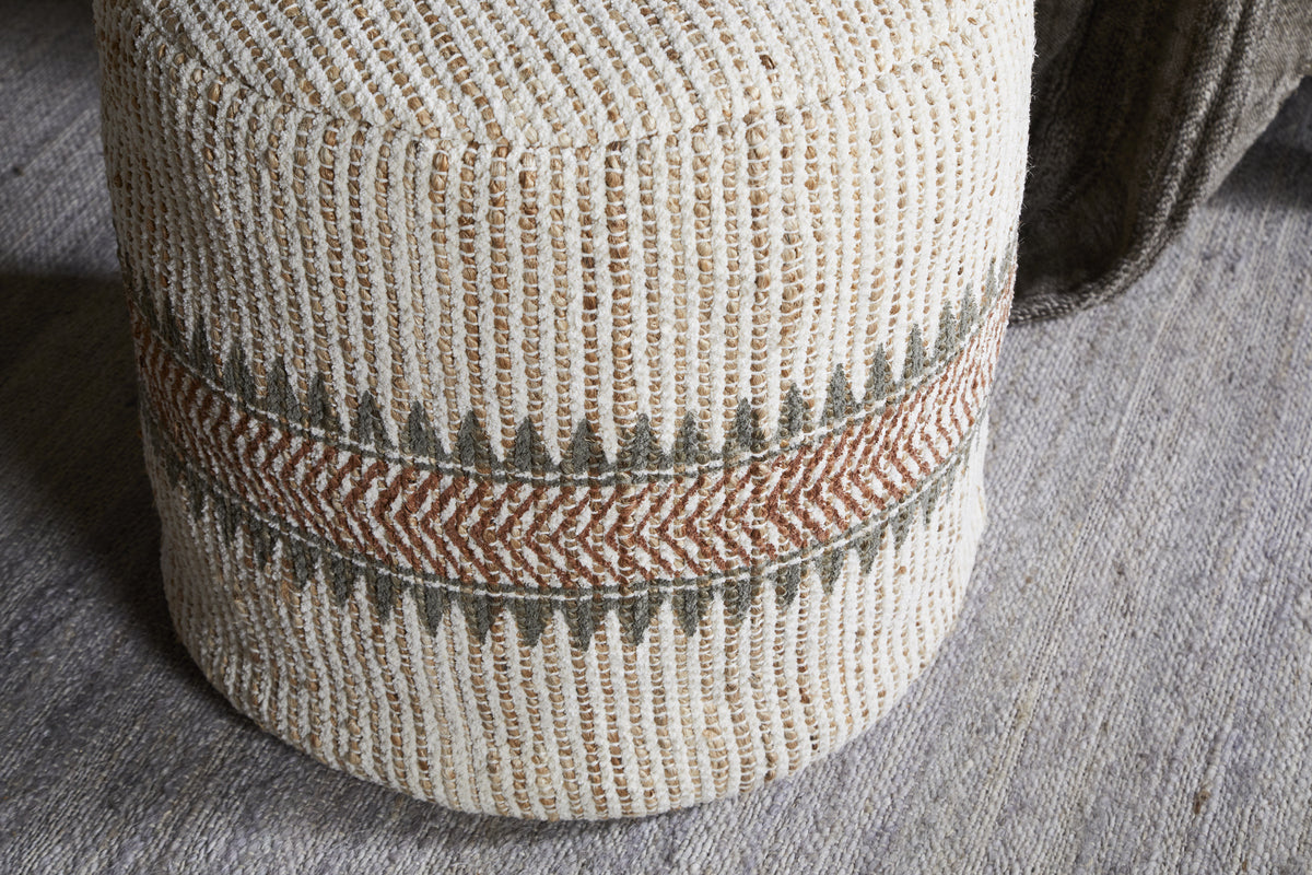 The nkuku Zairya Jute & Cotton Tall Pouf in Natural & Rust features textured, woven fabric with vertical beige and brown stripes and a central zigzag band of olive green and rust chevrons, shown on a gray woven rug.