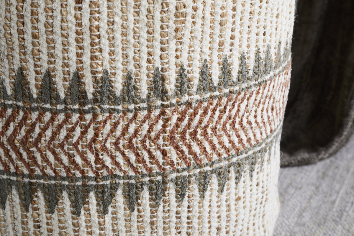Close-up of the nkuku Zairya Jute & Cotton Tall Pouf in Natural & Rust, featuring a cream background, textured vertical stitches, a central zigzag in brown and gray, and rows of pointed gray shapes. The thick fabric looks soft and durable.