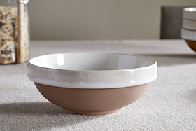 The nkuku Edo Dinnerware Set - Terracotta (Set of 12) features a ceramic bowl with a matte brown base and glossy off-white rim, styled on a beige tablecloth for an elegant, minimalist look in your tableware collection.