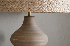 The nkuku Dalat Ceramic Table Lamp - Natural features a handcrafted design and white shade, bringing elegance to any room.