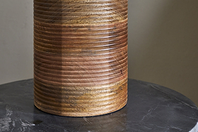 The Agua Grooved Table Lamp - Natural by nkuku features hand-grooved mango wood with horizontal grooves and a smooth, glossy finish. Its unique grain and warm color variations add texture atop a dark, veined marble surface.