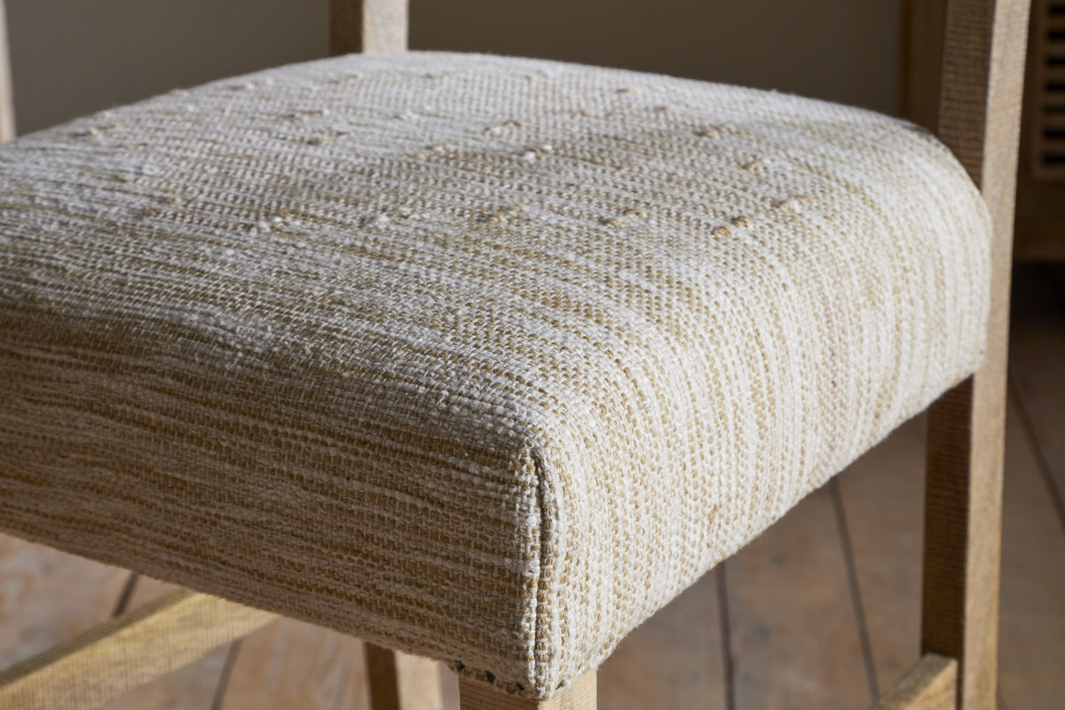 Close-up of the Zoha Cotton & Jute Upholstered Counter Chair by nkuku, featuring tightly woven natural upholstery with subtle stripes and tufted details, set on mango wood legs and frame atop a light wooden floor.