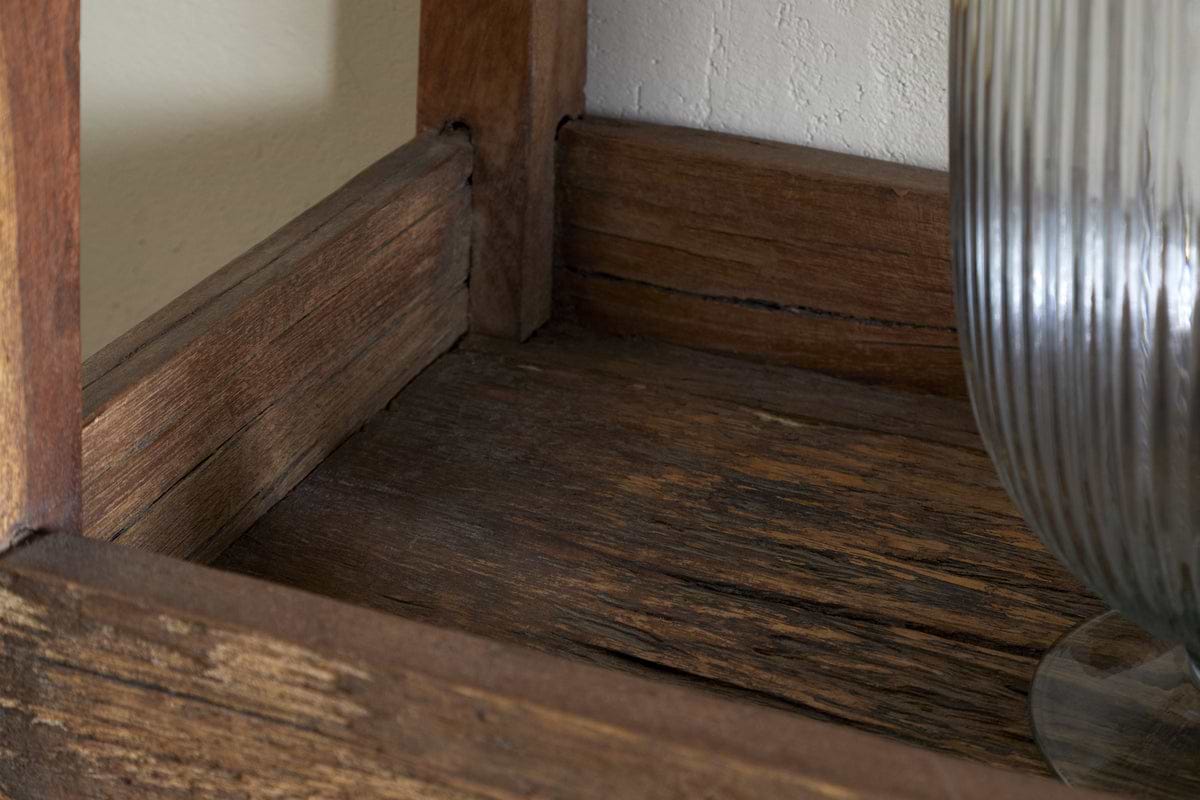 A close-up of the Akara Reclaimed Wood Storage Caddy - Natural by nkuku, showing its weathered, textured reclaimed wood and visible grain. On the right, a tall ribbed clear glass vase stands against a white wall with subtle shadows.