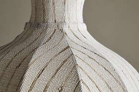 Close-up of the Kela Fabric Pendant in Off White by nkuku, featuring textured fabric and subtle brown accents. Its curved panels and raised details evoke a calming, linen-inspired ambience in soft, neutral tones.