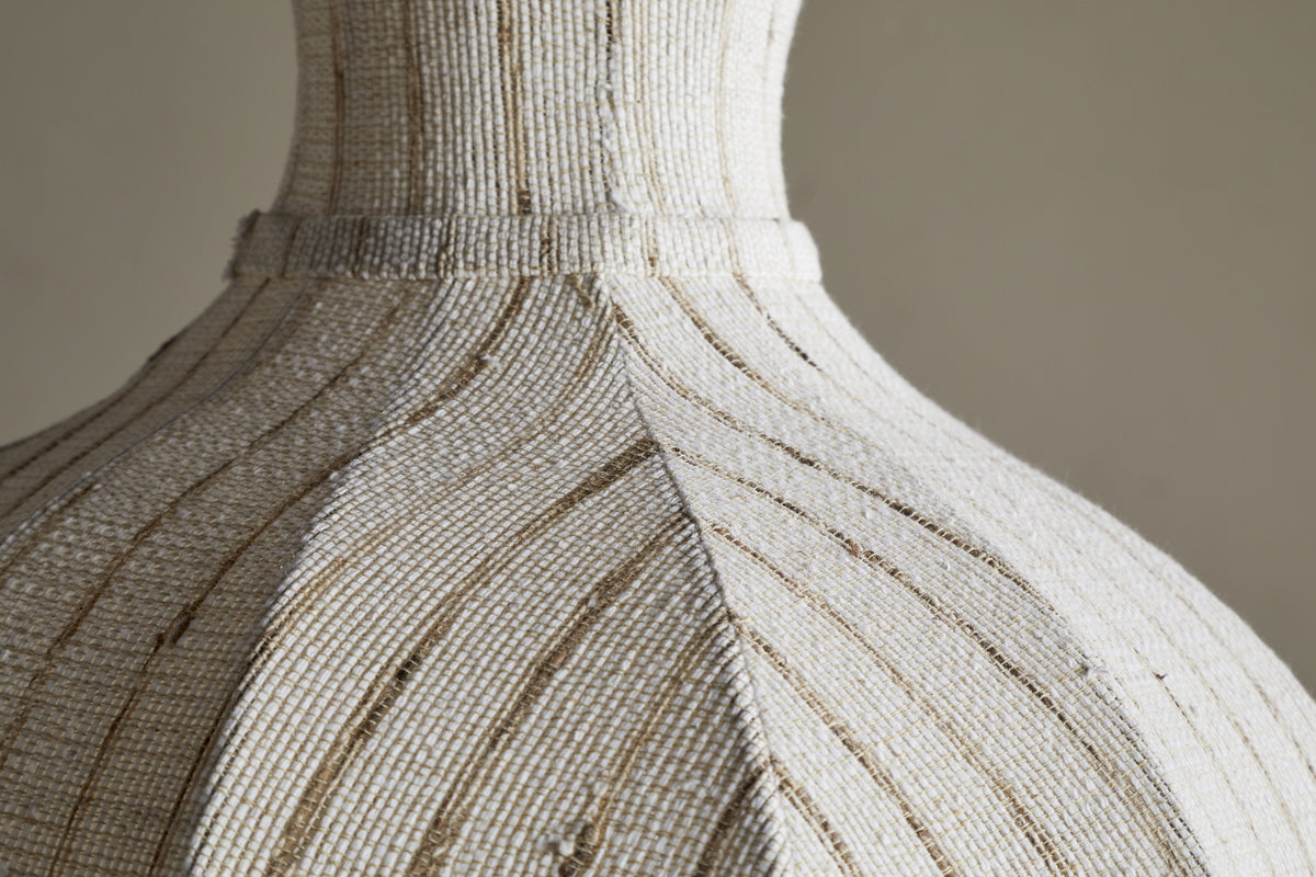 Close-up of the Kela Fabric Pendant in Off White by nkuku, featuring textured fabric and subtle brown accents. Its curved panels and raised details evoke a calming, linen-inspired ambience in soft, neutral tones.