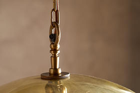 Close-up of the Otoro Recycled Glass Pendant - Honey - Large Round by nkuku, showcasing its elegant brass fittings and hanging hardware, which includes a brown rope, metal hook, and screw. The dome-shaped pendant is crafted from recycled glass with a honey-tinted finish that softly reflects light. The background is blurred in neutral tones, creating a warm ambiance.