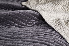 A close-up of the nkuku Nidra Velvet & Linen Bed Quilt - Charcoal, featuring soft gray cotton velvet on one side, cream linen on the reverse, and detailed Kantha stitching—ideal for King and Super King beds.