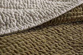 Close-up of two quilted layers—light cream and moss green—highlighting the soft, padded surface and stitched ridges of the nkuku Nidra Velvet & Linen Bed Quilt, crafted in cotton velvet style for king size bedding.
