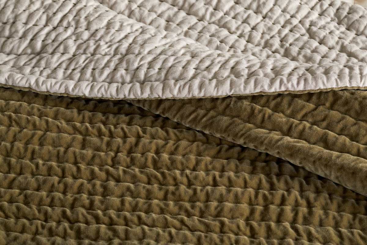 A close-up of the nkuku Nidra Velvet & Linen Bed Quilt in Moss, featuring textured cotton velvet with Kantha quilting and gathered stitching, plus a smooth, cream linen underside.