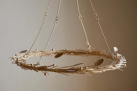 The Natesa Hanging Wreath - Brass by nkuku features delicate, light-hued twigs and brass leaves suspended by fine wires, highlighting traditional artistry and casting gentle shadows on any neutral wall.