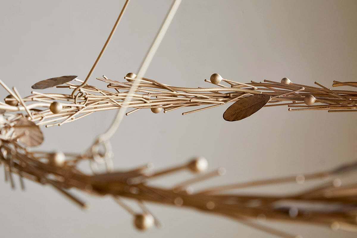A close-up of the Natesa Hanging Wreath by nkuku, an elegant piece crafted from brass with interwoven design elements, showcasing traditional craftsmanship against a neutral background.