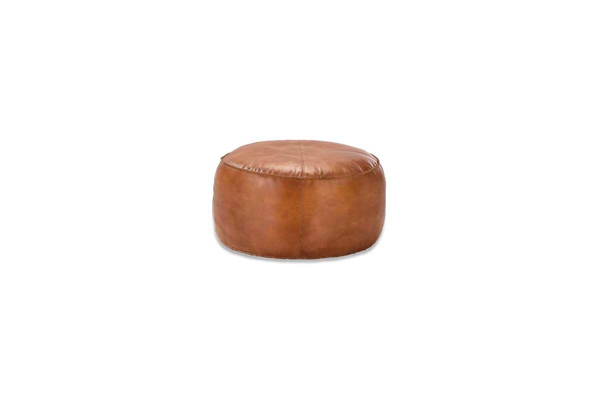 The Nadu Leather Pouf - Aged Tan by nkuku is a round, aged tan leather ottoman with visible stitching, shown on a white background. This modern piece offers a smooth finish and functions as extra seating or a stylish footrest.