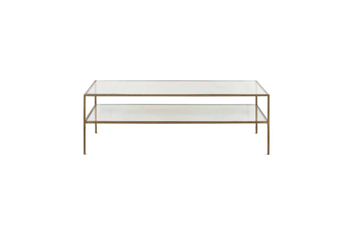 The Nakuru Iron & Glass Coffee Table by nkuku features a modern rectangular design with a slim gold metal frame, two clear glass surfaces (a top and lower shelf), and four slender legs, shown against a plain white background.