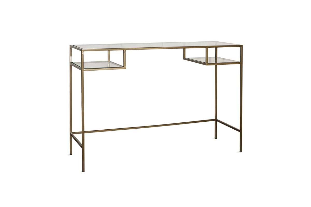 The Nakuru Iron & Glass Console Table by nkuku features a slender metallic gold frame and clear glass top, with two lower glass shelves. Its spaced legs and brass finish give it an airy, modern style—ideal as a hallway console table.