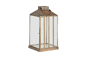 The nkuku Nampo Lantern - Aged Antique features clear glass panels, a weathered bronze frame, flat top, round handle, and a front hinged door for candles—ideal for vintage-style decor.