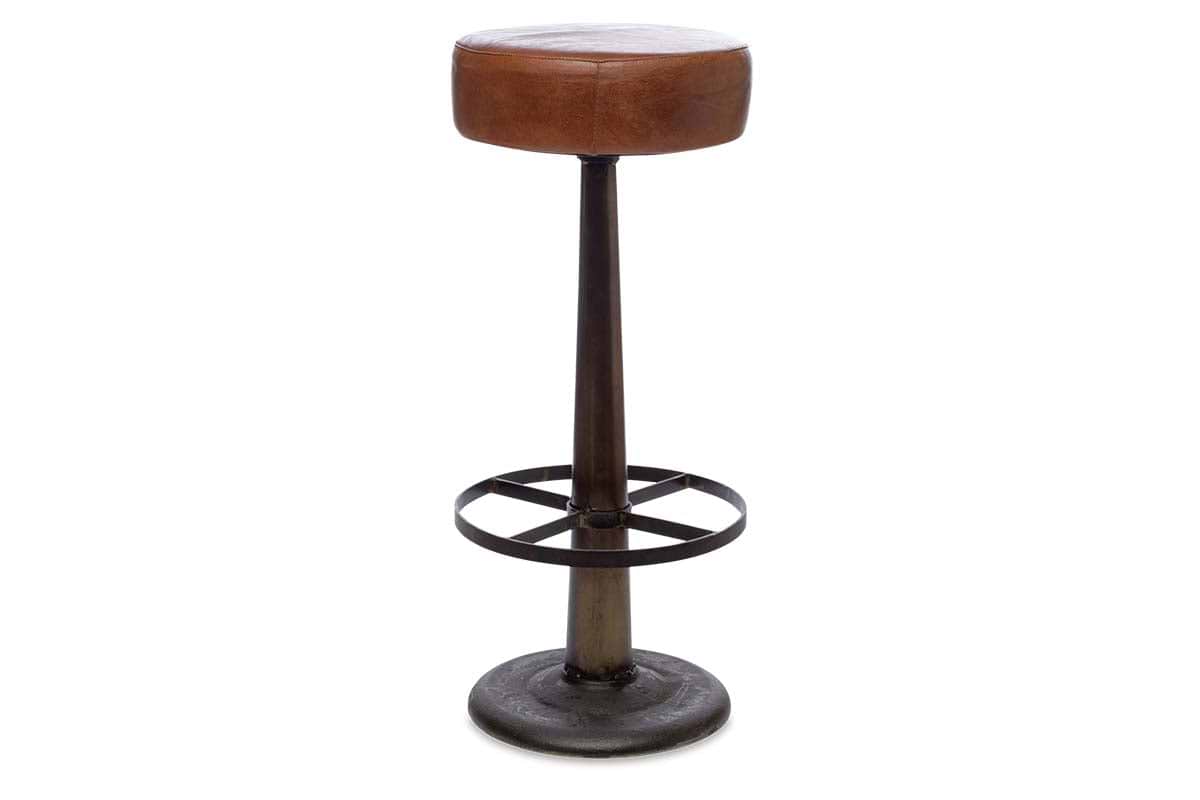 The Narwana Leather Round Stool - Aged Tan by nkuku features an aged tan leather seat, single dark metal pedestal base, and circular footrest. This counter stool has an industrial, minimalist design set against a white background.