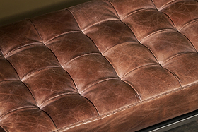 Close-up of the Nasan Leather Upholstered Bench by nkuku, featuring a tufted tan leather cushion with visible stitching and creases. Its grid pattern adds texture and plush comfort, giving a versatile look suitable for any setting.