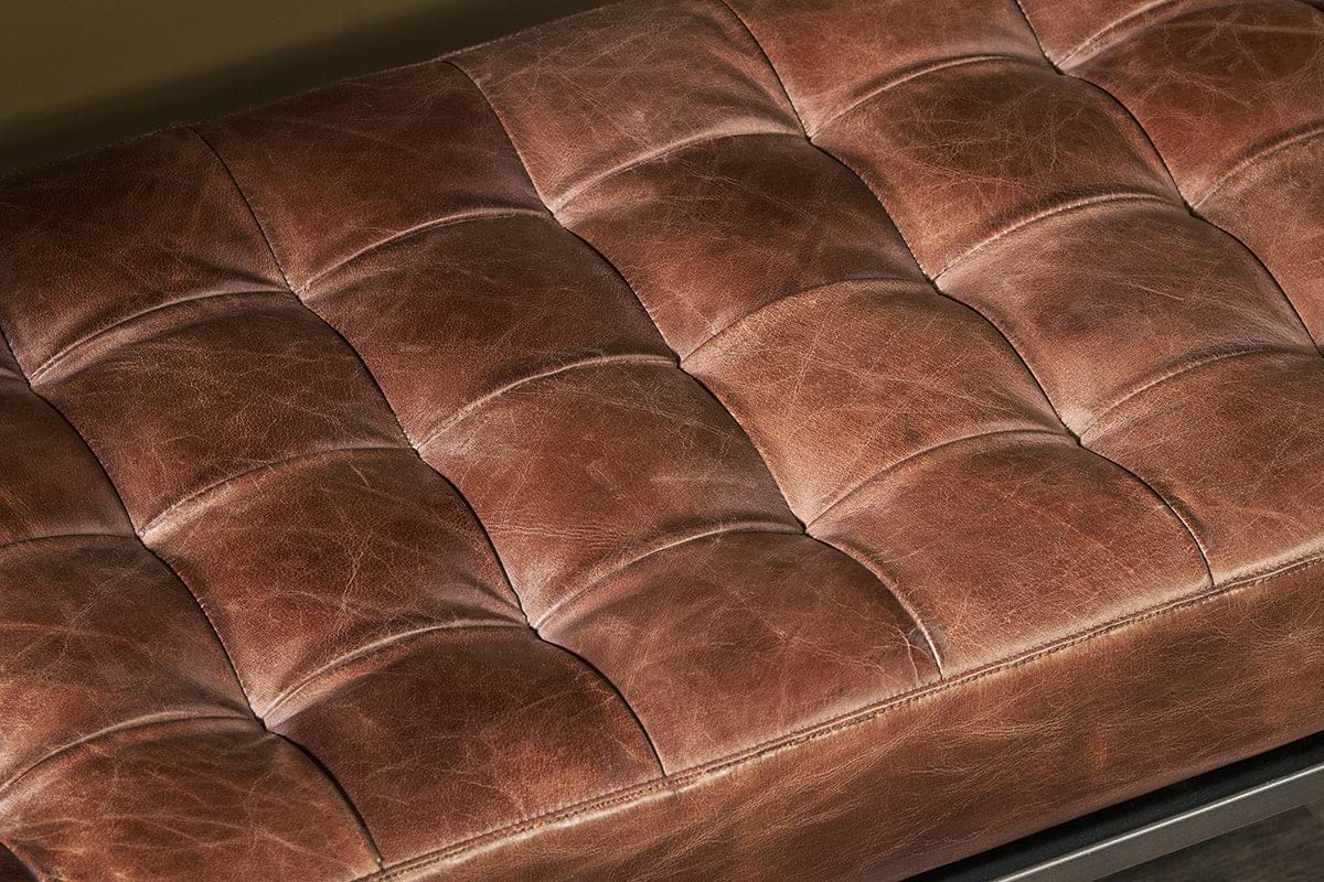 Close-up of the Nasan Leather Upholstered Bench by nkuku, featuring a tufted tan leather cushion with visible stitching and creases. Its grid pattern adds texture and plush comfort, giving a versatile look suitable for any setting.
