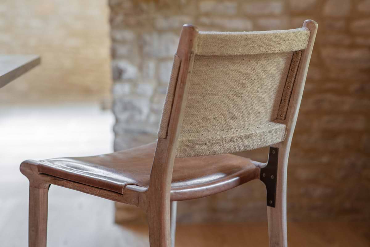 Close-up of nkuku's Nayan Leather & Jute Counter Chair - Tan, featuring a wooden frame, brown leather seat, jute backrest, and a metal bracket connecting the back to the chair leg.