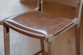 Close-up of the Nayan Leather & Jute Counter Chair by nkuku showcases its tan leather seat and jute weave. The detailed craftsmanship stands out, while the blurred background accentuates the chair’s natural textures and quality materials.