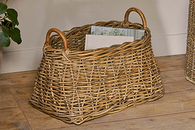 The Netra Rattan Basket - Natural by nkuku, with rounded handles, sits on a wooden floor holding two books—a stylish decorative storage basket or hallway organiser for any space.
