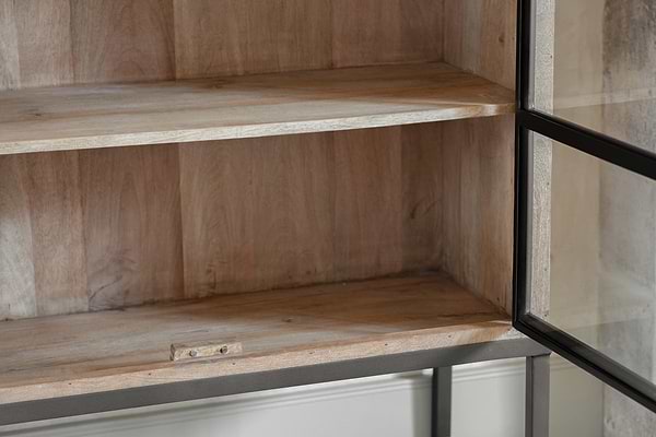 Close-up of empty wooden shelves inside the Nirvi Wood & Iron Cabinet - Black by nkuku. This cabinet blends an industrial look with natural mango wood, a sturdy black metal frame, and a small latch at the bottom for a clean, well-crafted finish.