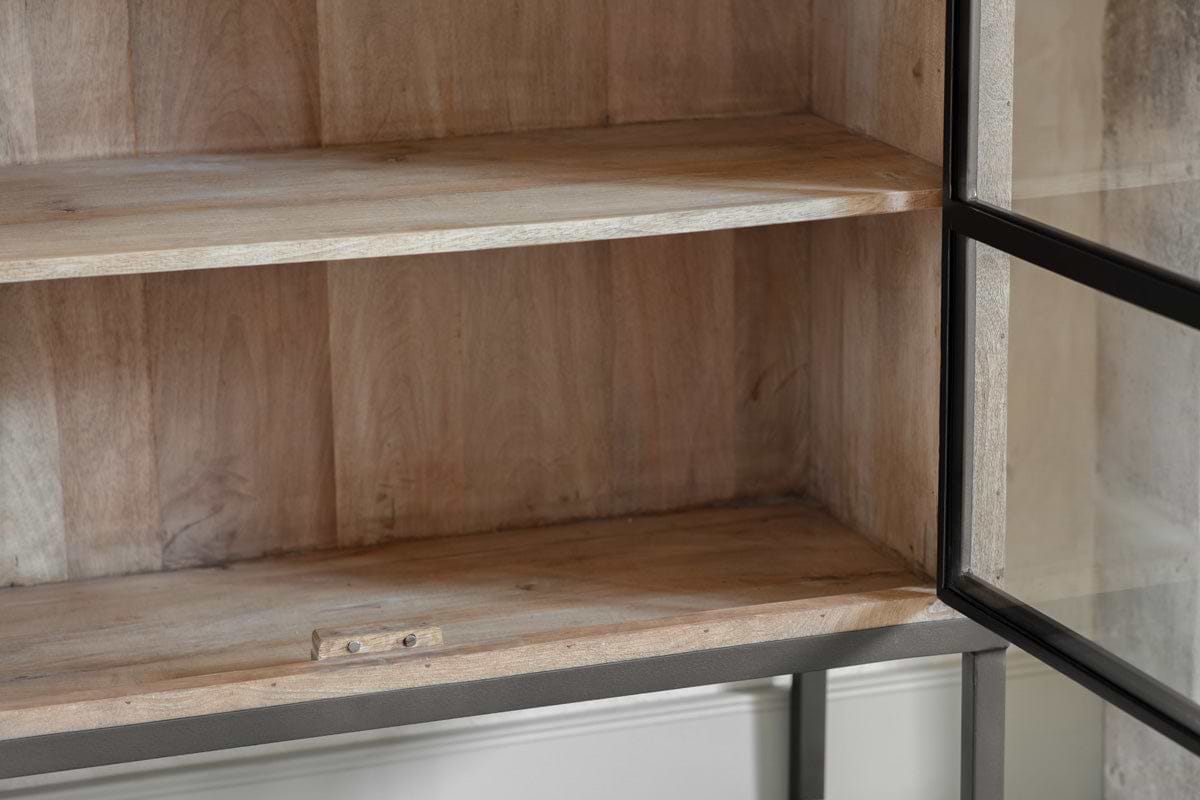 Close-up of empty wooden shelves inside the Nirvi Wood & Iron Cabinet - Black by nkuku. This cabinet blends an industrial look with natural mango wood, a sturdy black metal frame, and a small latch at the bottom for a clean, well-crafted finish.