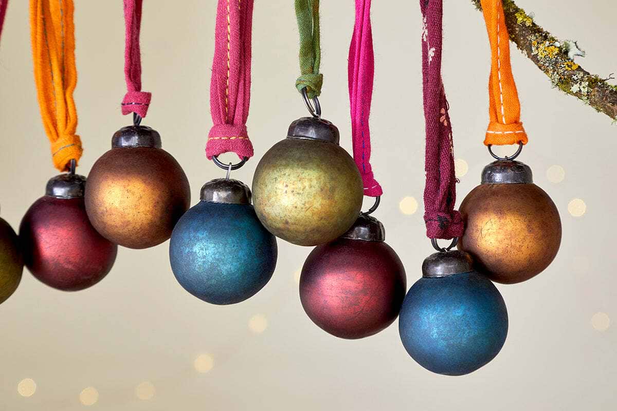 The nkuku Oko Mini Baubles - Mixed Matt (Set of 12) features twelve rustic matte ornaments in vibrant shades of orange, gold, red, blue, and green, each hanging from fabric ribbons—perfect for adding color to your festive décor.