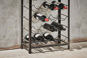 The nkuku Obra Industrial Wine Rack – Mango Wood & Iron (Large) holds 12 bottles in four rows, with dark brown iron and wood blending modern style and classic charm against a textured gray wall.