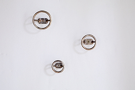 Three Olani Bathroom Hooks by nkuku in antique brass are mounted on a plain white wall in a loose triangular formation, casting soft shadows and creating a subtle, spa-like ambiance.