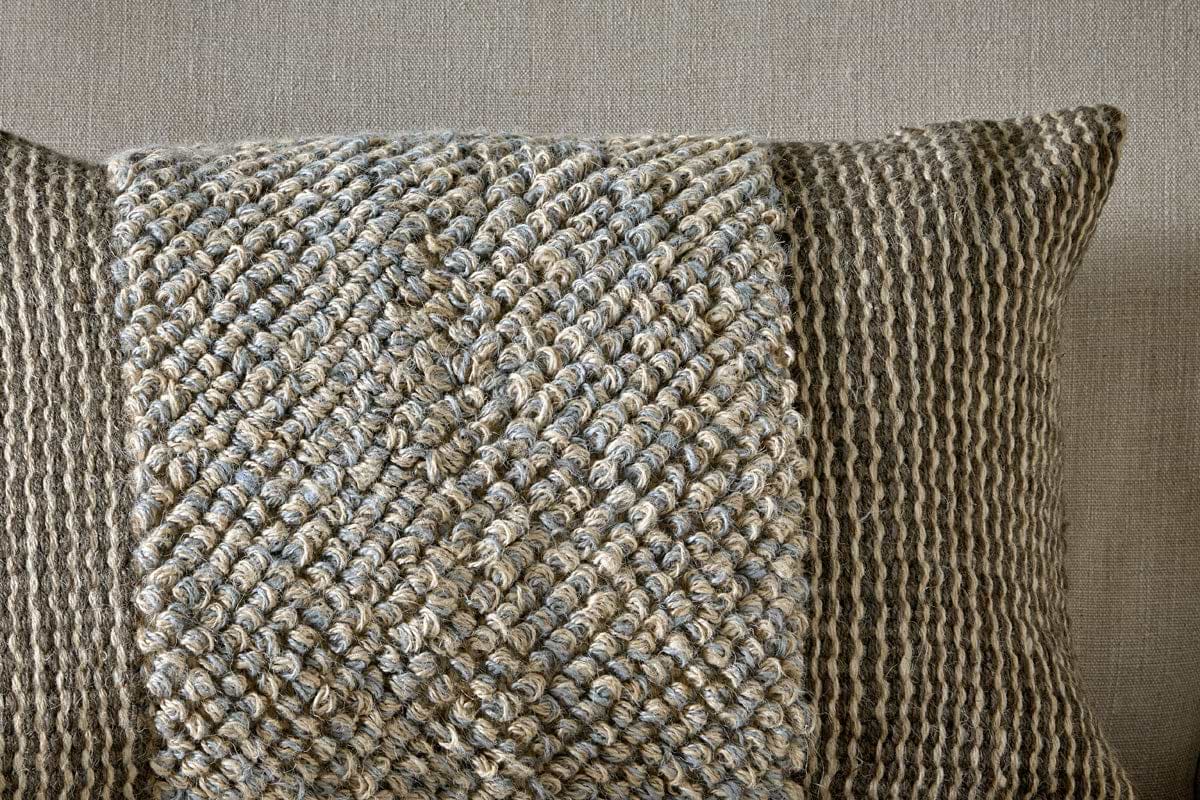 The nkuku Paduna Jute & Cotton Cushion Cover in Soft Blue & Brown features a textured, woven blend with a central braided panel and vertical stripes in beige and gray on a neutral background.
