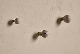 Three Paladi Marble & Iron Round Hooks - Grey by nkuku, with spherical hand-carved stone and brass stems, are spaced on a textured beige wall. Each hook casts a soft shadow, accentuating their minimalist contemporary look.