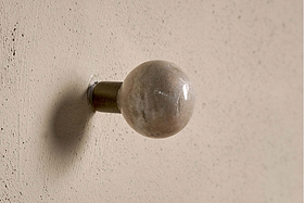 The nkuku Paladi Marble & Iron Round Hook in Grey features a glossy taupe and ivory marble knob on a short metallic base, mounted on a textured beige wall with soft lighting casting a subtle shadow.