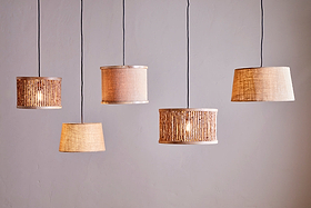 Five nkuku Dia Jute Lampshade - Natural pendant lamps hang against a plain, light wall. Each showcases unique woven or jute styles and shapes, adding warm ambient light and textured, cozy charm to modern décor.