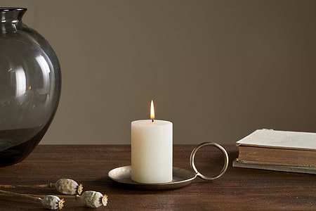 The Rustic Soy Blend Mini Pillar Candle - White by nkuku features a textured finish and sits elegantly on the table, adding charm to any setting.