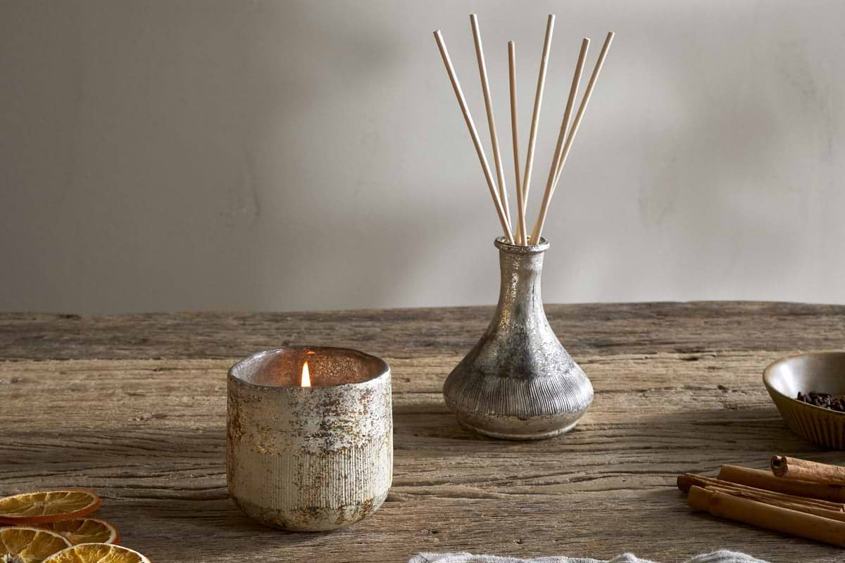 A cozy display featuring nkukus Mandarin & Clove 1 Wick Scented Candle in a textured holder, paired with a small reed diffuser vase, dried orange slices, and cinnamon sticks for festive charm.