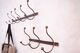 Two nkuku Rama Iron Hook racks—one with five hooks, one with three—are mounted on a light, textured wall. Each features curved iron hooks with ball tips, and a bag with dark handles hangs from the larger rack. Perfect for hallway storage.