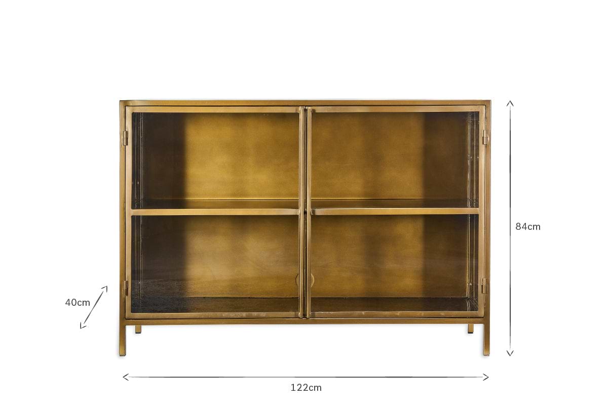 The nkuku Ranchi Iron Sideboard is a rectangular gold metal cabinet with two glass doors, four internal sections, and slim legs. Dimensions: 84 cm (H) x 122 cm (W) x 40 cm (D). Photographed against a white background.
