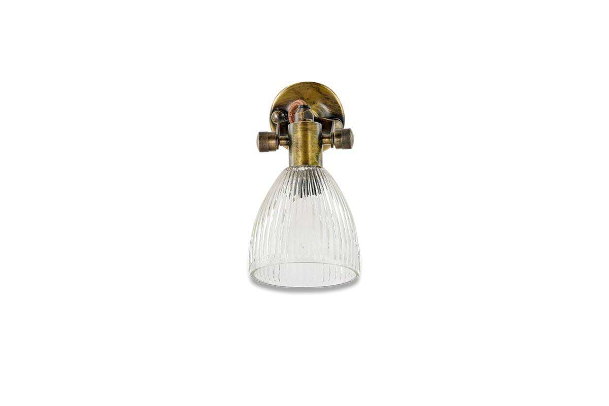 The nkuku Rarni Recycled Glass Single Wall Light features a vintage-style brass fixture and an oval mount that supports a downward-facing, ribbed clear glass shade, blending classic charm with sustainable materials.