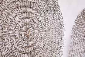 Close-up of the nkuku Rayan Wire Wall Art in Antique Brass, showcasing two large, circular sculptures with concentric rings and lacy geometric patterns. Only part of the second piece is visible on a light-colored wall.