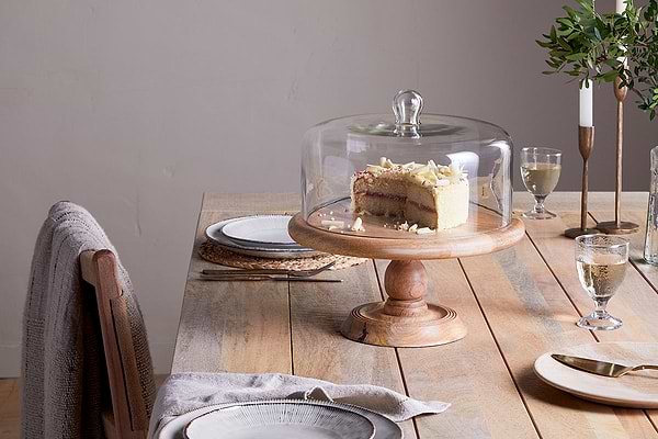 The nkuku Recycled Glass Dome Cake Stand with a mango wood base is perfect for displaying and storing treats in style.