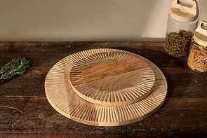 Two nkuku Soria Chopping Boards, hand carved from mango wood, are stacked on a rustic table with glass jars of pasta and herbs to the right and fresh rosemary to the left, all bathed in soft, warm light.