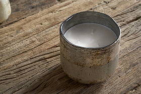The nkuku Juniper & Fir 3 Wick Scented Candle, with a bespoke fragrance, sits in a rustic textured ceramic holder on a weathered wooden surface.
