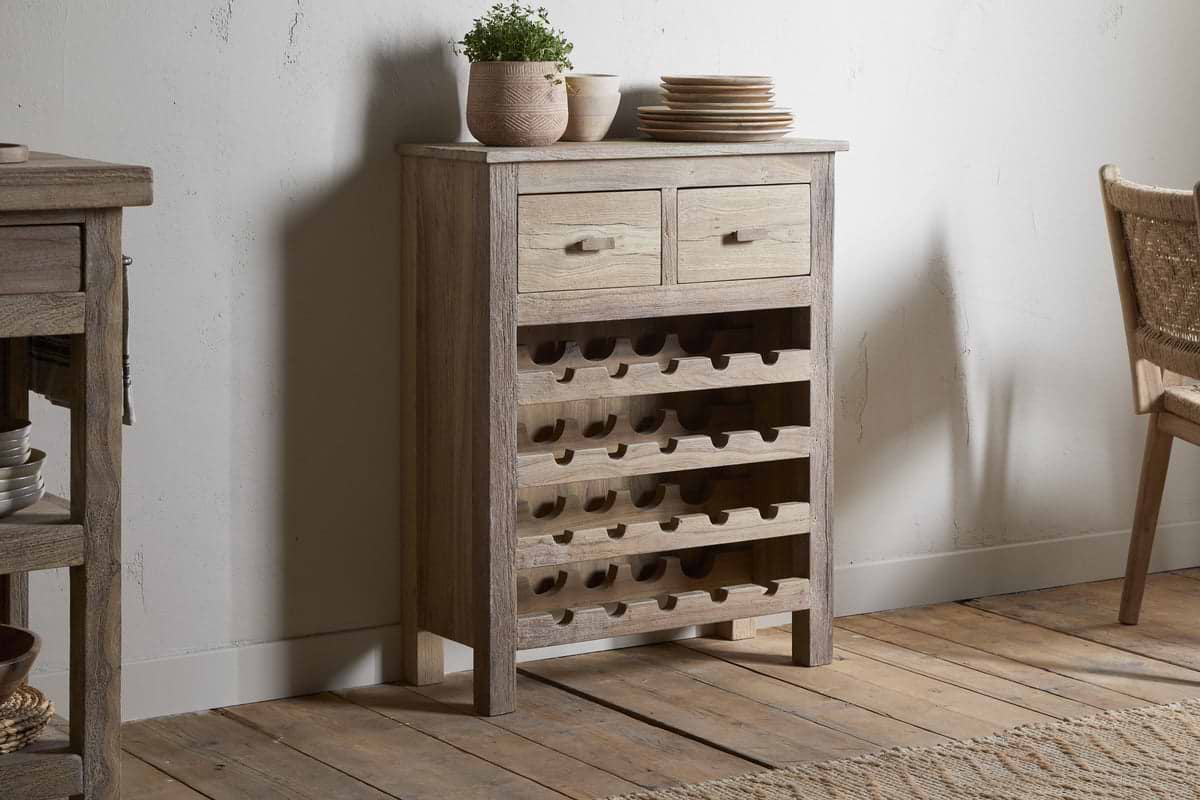 The Shanthi Reclaimed Wood Wine Rack - Natural by nkuku features two top drawers and spacious storage for wine bottles, dishes, or décor. It stands against a light wall on wooden flooring in a cozy setting.